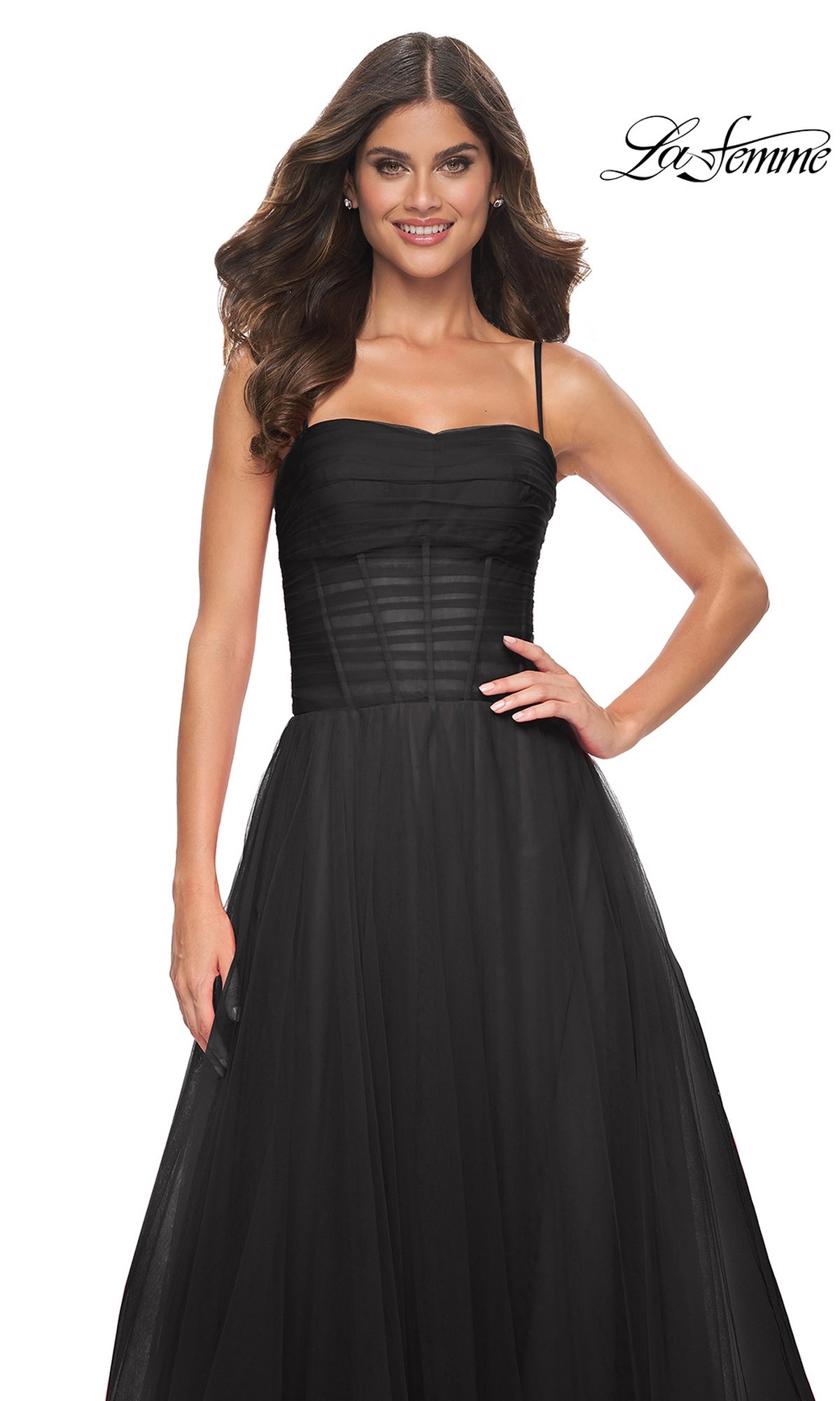 A woman smiles in the La Femme Sheer-Waist Long Prom Ball Gown 32017—sleeveless, black, with a fitted bodice and tulle skirt—standing against a white background.